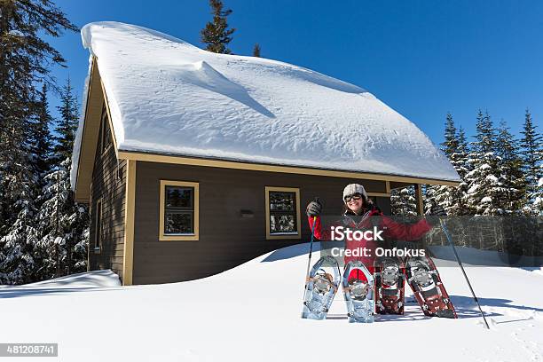 Woman With Snowshoes And Wooden Chalet In Powder Snow Stock Photo - Download Image Now