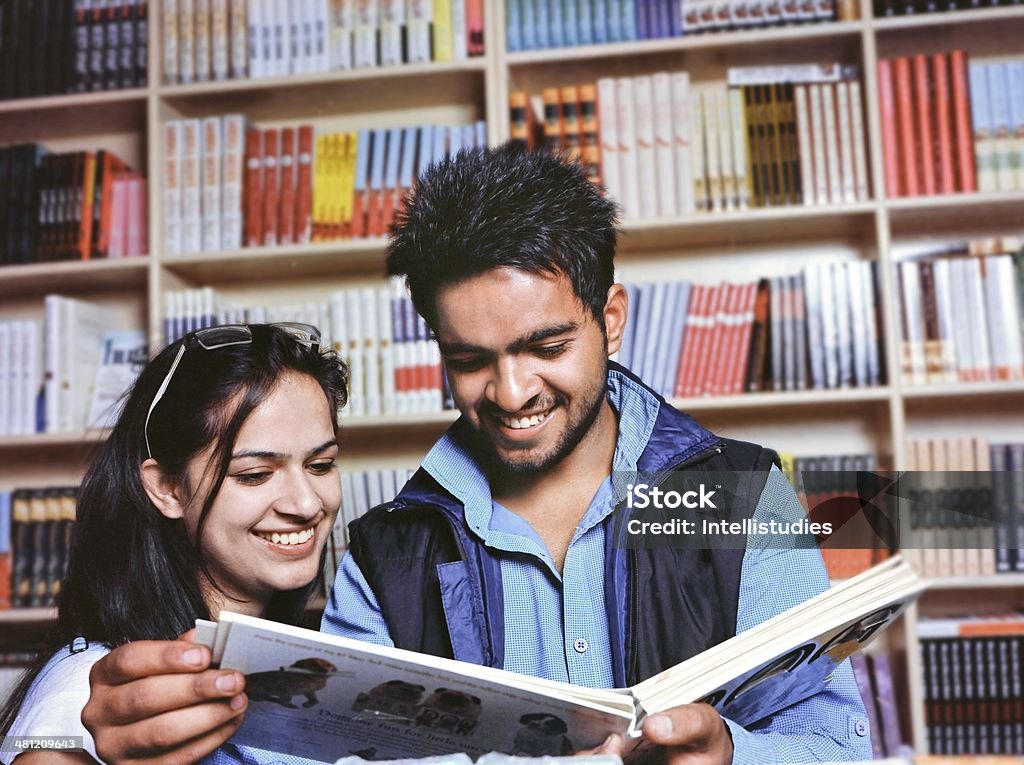 Two cheerful youth studying book in the university library. Group of Indian / Asian college students reading a book in the college library. Student Stock Photo