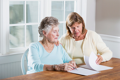 Mature woman (60s) helping elderly mother (90s) with paperwork.