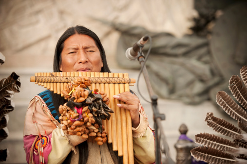 Venice, Italy - March 3, 2014: Peruvian musician with long hair playing on a traditional musical instrument named flute de pan on Piazza San Marco at sea side. The musician wearing wearing national costumes with plume. Venice, Italy.