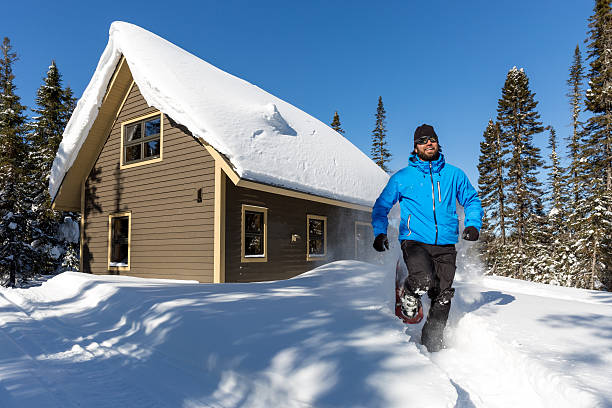 running homme avec raquettes et chalet en bois dans la poudreuse - winter snowshoeing running snowshoe photos et images de collection