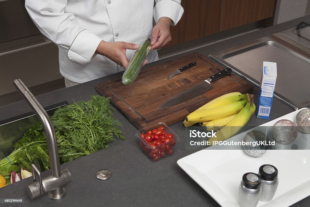 Chef Unwrapping Cucumber At Kitchen Counter Midsection of male chef unwrapping cucumber at commercial kitchen counter Adult Stock Photo