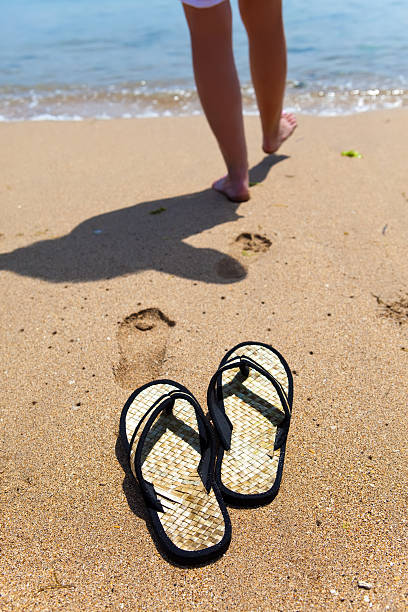 istock Beach slippers on sand, and female feet at  sea edge 481237170