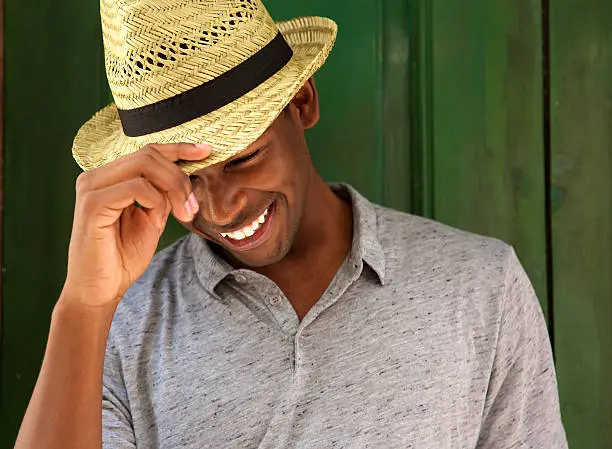 Close up portrait of a happy young man laughing with hat and looking down
