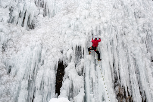 An adventurous  fixing the ice axe on ice-covered rock face during ice climbing.