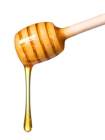 Honey dripping from wooden honey dipper isolated on white background