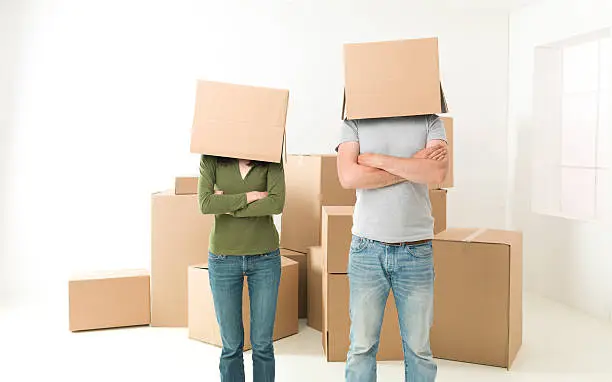 couple with boxes on their heads standing in their new house, arms crossed against their chests