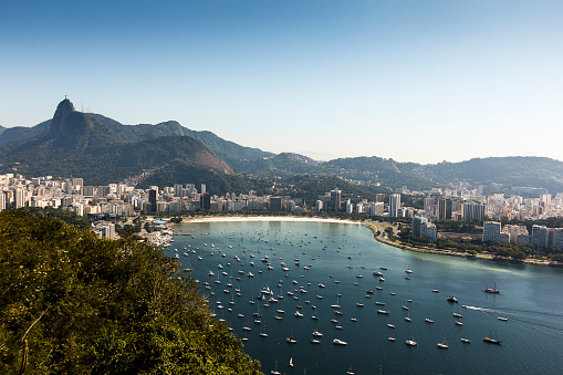 A DSLR photo of Rio de Janeiro, Brazil, july 2015. In the middlegroung there is Botafogo beach and its marina full of boats. In the background, there is Corcovado Mountain with Christ the Redeemer statue. It is a bright sunny day with cloudless blue sky.