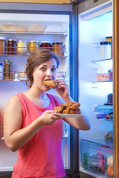 istock Woman Eating Unhealthy Fried Chicken in Front of Open Refrigerator 481274508