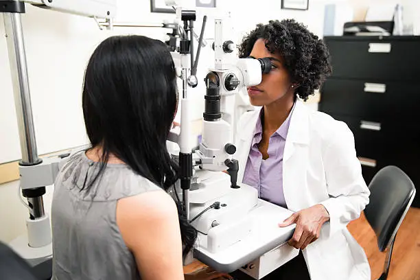 Optometrist in exam room with a patient looking into microscope machine. 