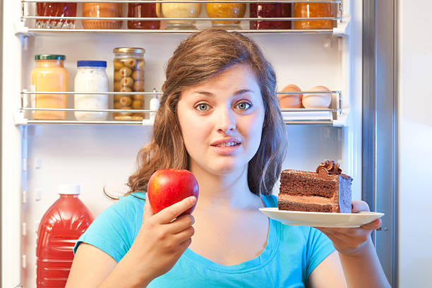 istock Woman Choosing Between Healthy or Unhealthy Snack by Open Refrigerator 481277952