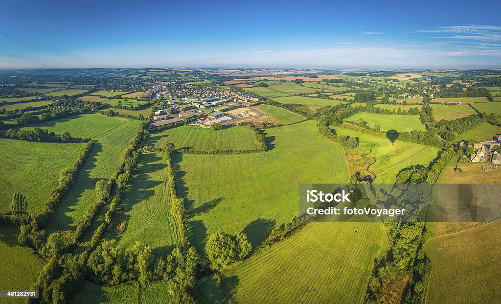 Country town in patchwork pasture landscape summer green fields panorama Picturesque patchwork landscape of green pasture and golden crops, rolling hills, farms, villages and country towns beneath clear blue summer skies. ProPhoto RGB profile for maximum color fidelity and gamut. Aerial View Stock Photo