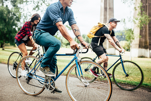 A mixed-race group of friends commuting in an urban city environment with trees in background. This happy trio is excited for their fun adventure.  Horizontal with copy space.  Three people riding their bicycles.