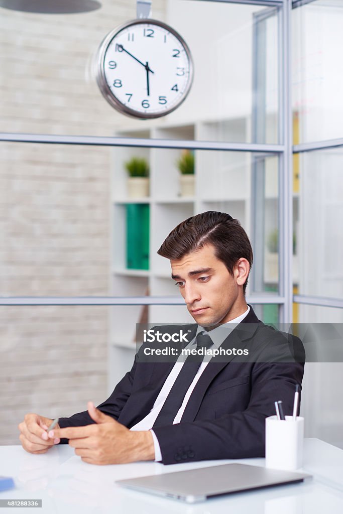 Being bored at office Young businessman being bored at office at ten minutes to six 2015 Stock Photo