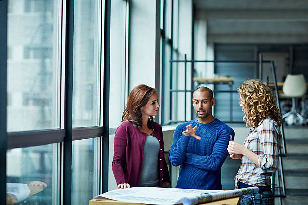 Casual discussion between coworkers Casual discussion between coworkers at high table by window in modern studio business casual stock pictures, royalty-free photos & images