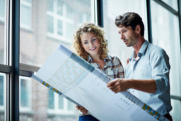 Two architects checking blueprint Two architects checking blueprint by window in modern studio architect stock pictures, royalty-free photos & images