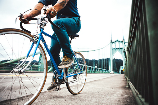 An unrecognizable man commuting across the St John's Bridge in an urban city environment. He travels on his street bicycle into the city over the Saint John's Bridge. No face visible. Horizontal with copy space.