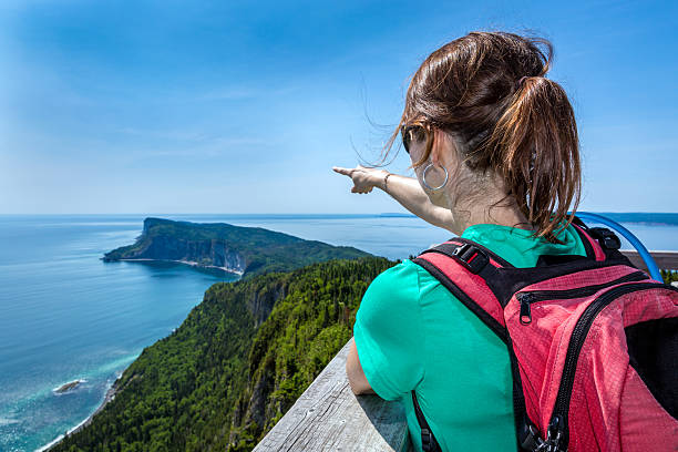 Woman on Mountain Summit Pointing a Direction Woman hiker wearing a backpack on a Mountain Summit and Pointing a Direction and the ocean. She is pointing the Gaspé Peninsula in Forillon, Quebec, Canada. forillon national park stock pictures, royalty-free photos & images