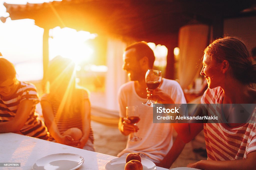 Here's to our friendship! Smiling friends spending some quality time during the dinner party, outside in a beach house, talking and laughing  Celebratory Toast Stock Photo