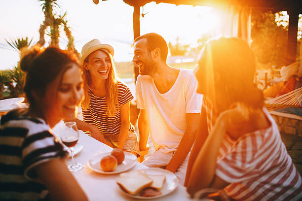 Seaside dinner party Smiling friends spending some quality time during the dinner party, outside on a beach, talking and laughing  evening meal stock pictures, royalty-free photos & images