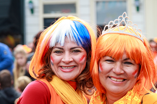Dordrecht, The Netherlands - April 27, 2015: Women dressed in orange laughing with painted faces on Hollands national Kings day celebrations in the old center of Dordrecht.