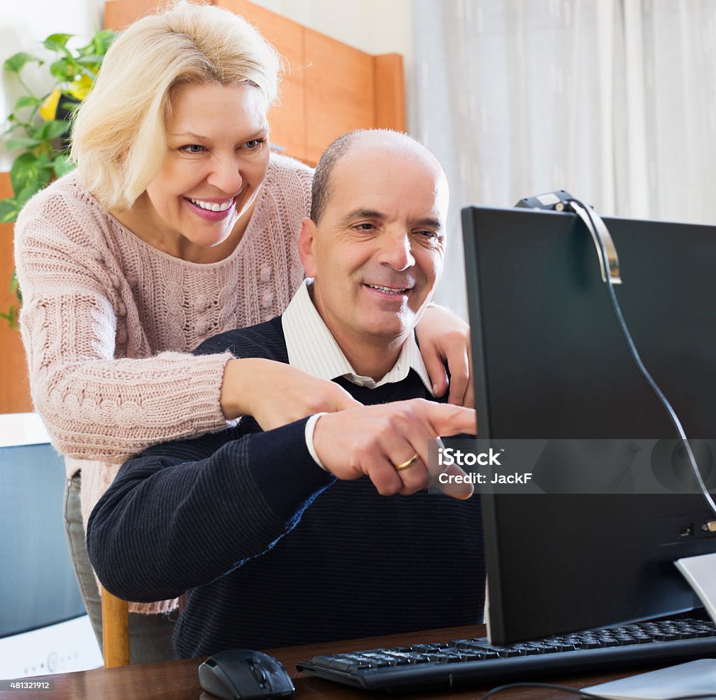 Couple talking with someone online Happy elderly couple talking with someone online and smiling at home 2015 Stock Photo