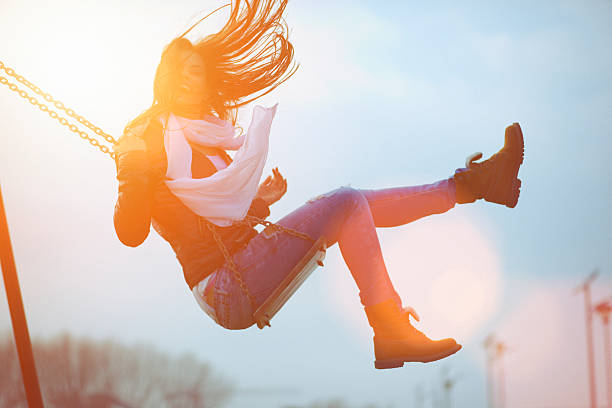 Young woman having fun swinging in sunlight. Shallow DOF. Shallow contrast and lens flare due to the sunlight from the back side.Developed from RAW; retouched with special care and attention; Small amount of grain added for best final impression; Ready made for print and web use; Adobe RGB color profile.