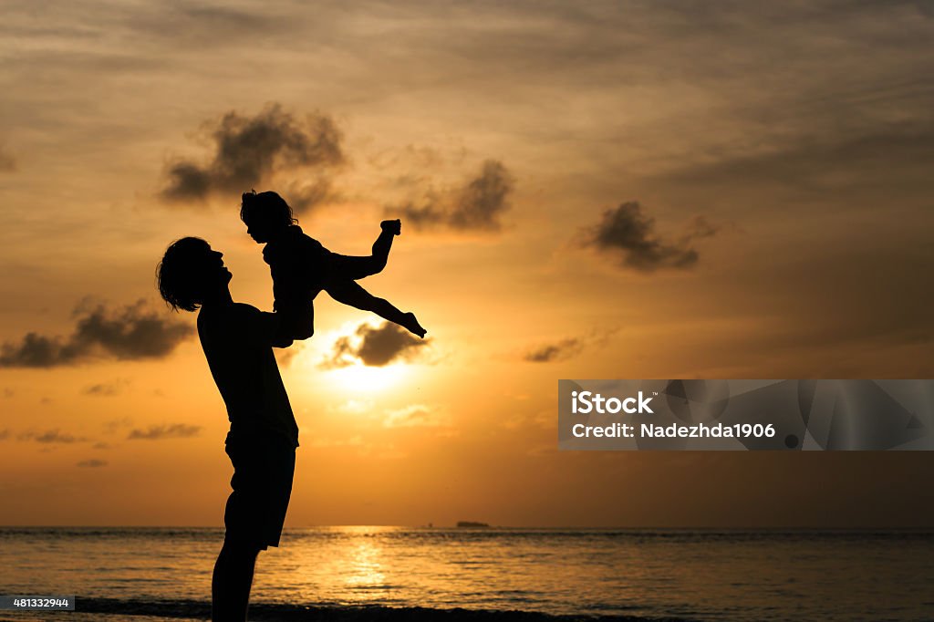 Father and little daughter silhouettes at sunset Father and little daughter silhouettes on beach at sunset 2015 Stock Photo