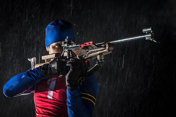 Athletic man holding biathlon rifle to fire and his finger on trigger.