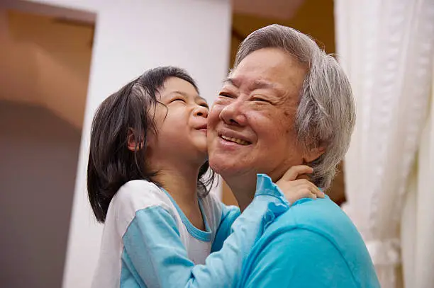 portrait of a grandmother being kissed by her granddaughter.