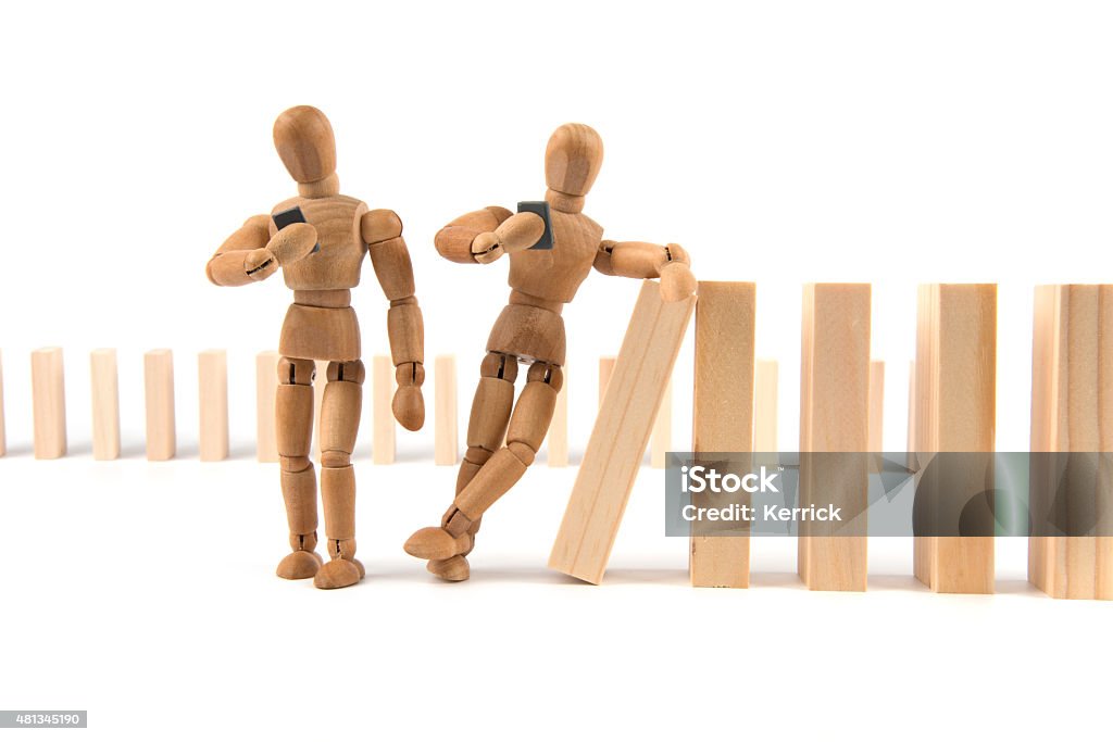 wooden mannequin leans careless on domino cascade with smartphone wooden mannequin leans careless on domino cascade - what happen next?  2015 Stock Photo