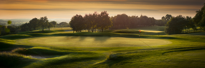 a panoramic scene of an empty golf course , with the shadows falling toward camera as the light fades .