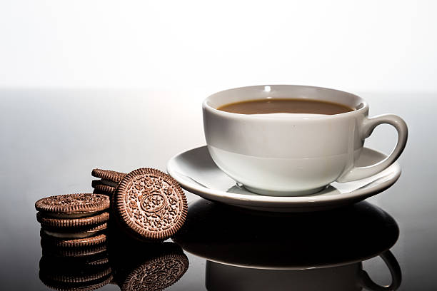 Creme-filled sandwich cookie and coffee on dark reflective background