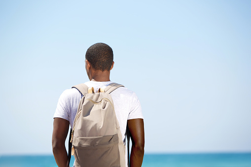 Rear portrait of a black man standing with backpack by the sea