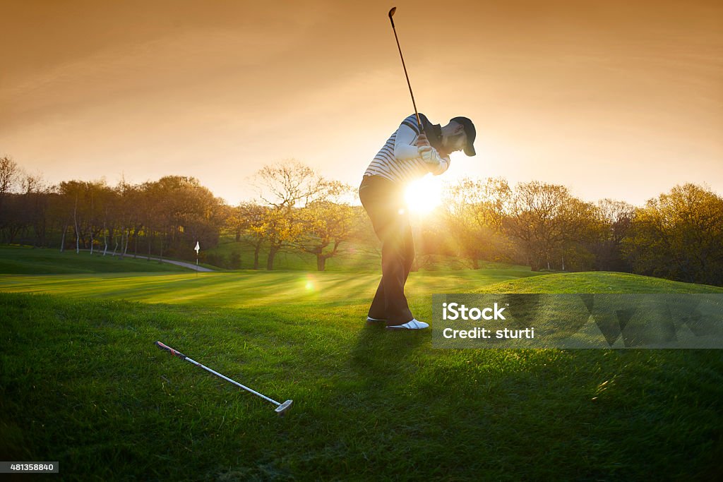 backlit golf course with golfer chipping onto green a lone golfer chips onto the green , the low sun is coming from behind him and flaring to camera. Golf Stock Photo