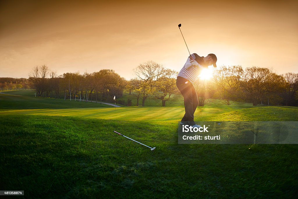 backlit golf course with golfer chipping onto green a lone golfer chips onto the green , the low sun is coming from behind him and flaring to camera. Golf Stock Photo