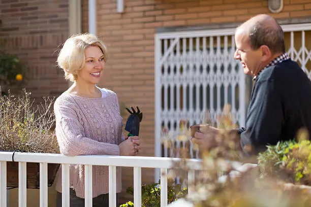 Mature smiling woman talking with male neighbor at balcon