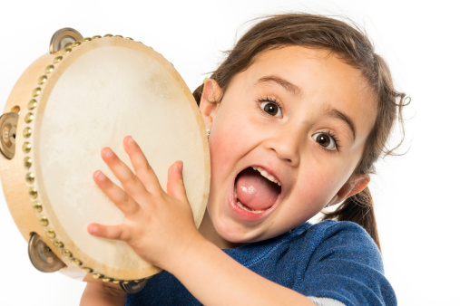 Smiling hispanic little girl posing looking at the camera playing tambourine