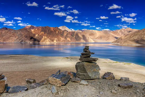 Rocks and reflection of Mountains on Pangong tso (Lake) with blue sky. It is huge lake in Ladakh, It is 134 km long and extends from India to Tibet. Leh, Ladakh, Jammu and Kashmir, India