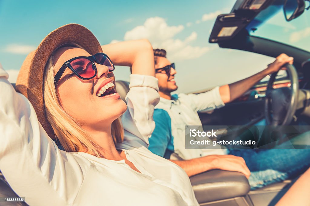 Freedom of the open road. Side view of joyful young woman relaxing on the front seat while her boyfriend sitting near and driving their convertible Car Stock Photo