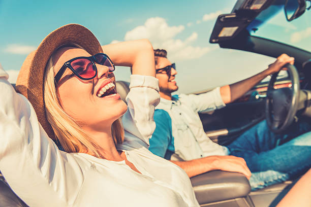 Freedom of the open road. Side view of joyful young woman relaxing on the front seat while her boyfriend sitting near and driving their convertible riding photos stock pictures, royalty-free photos & images