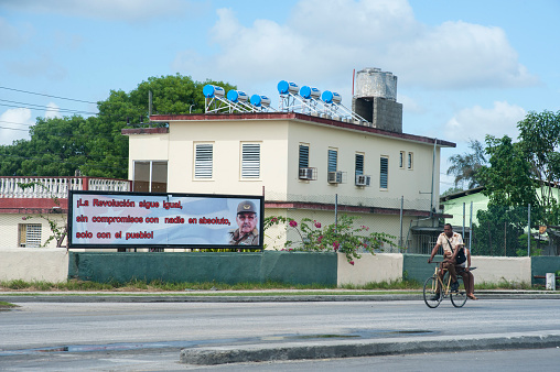 Havana, Cuba - May 17. 2015 A man rides his bicycle past a billboard featuring Raúl Castro