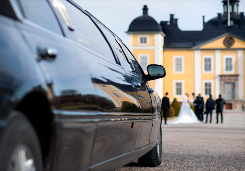Black limo waiting for bride and groom in front of mansion. Focus on reflection.