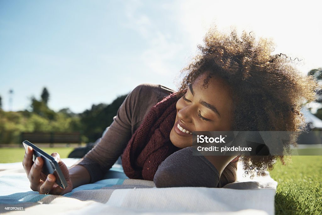 Sending flirty texts to my love Shot of a smiling young woman relaxing with her phone in the park Females Stock Photo