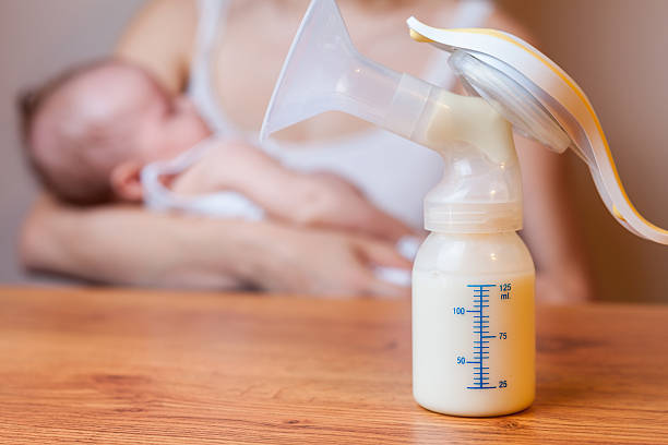 Manual breast pump with milk, mother and baby at background Manual breast pump, mothers breast milk is the most healthy food for newborn baby. Happy mother with baby at background breast milk stock pictures, royalty-free photos & images