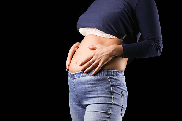 istock Woman with hands on small belly on black 481401362