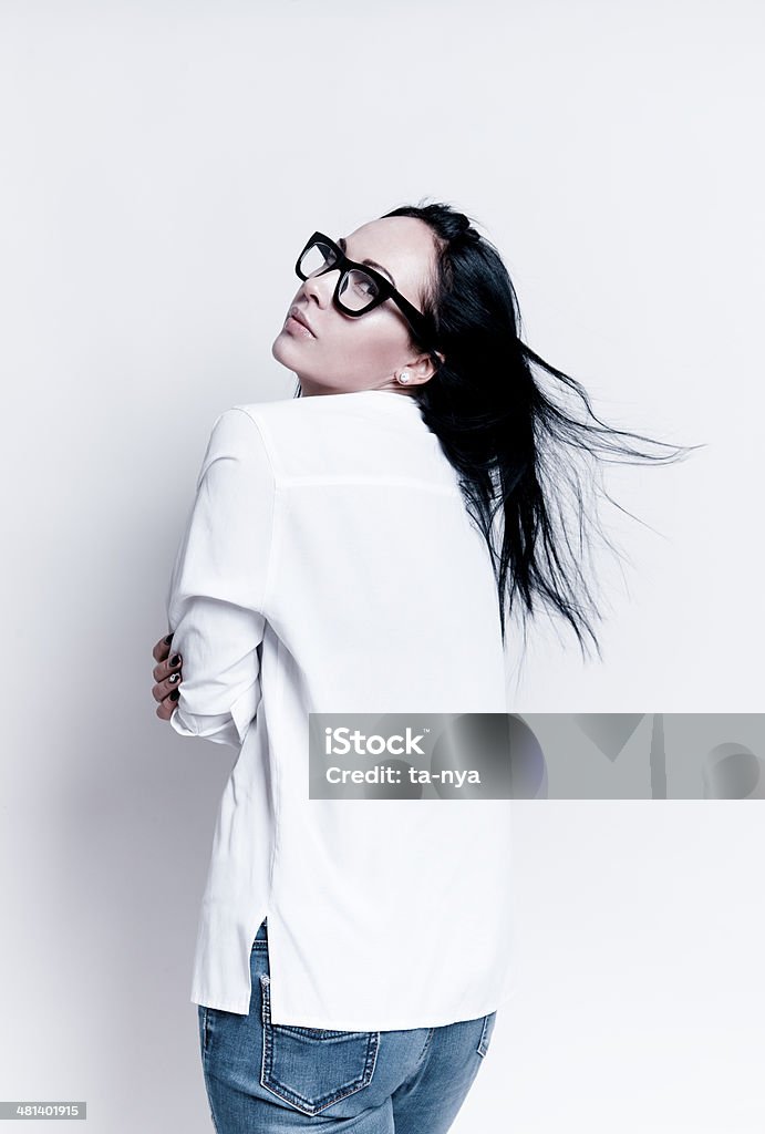 Beautiful woman in glasses Attractive woman with beautiful natural neutral make-up wearing white shirt,jeans,glasses and look from the back at the viewers. Fashion model studio portrait on light background. 30-34 Years Stock Photo