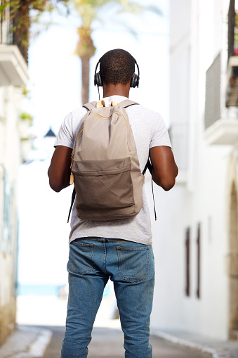 Portrait from behind of a young african american man with bag and headphones standing in the street