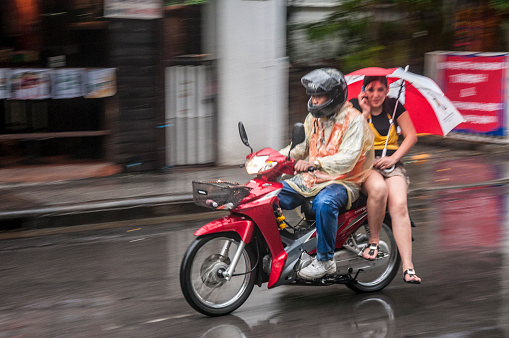 Bangkok, Thailand - May 29, 2012: A woman talking on the phone and using an umbrella whilst taking a motorcycle taxi in Nana Soi 4, Bangkok, Thailand