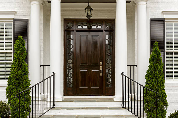 Dark front door with white columns A grand entrance way leading up to an ornate dark wood door with green trees. majestic stock pictures, royalty-free photos & images
